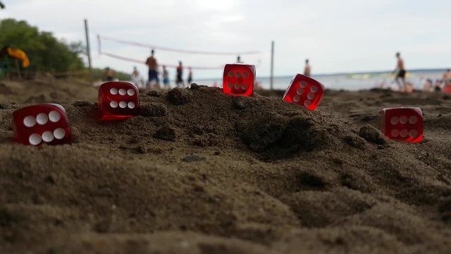 A view of big red dices lying on the seashore of Oka Beach, Great Montreal, Quebec, Canada with some guys playing beach volleyball in the background.Concept of leisure,creativity,relaxation.
