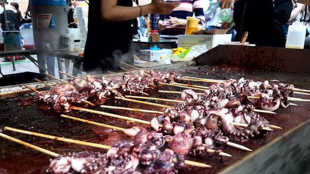 A man handling the octopus meat over the screws on a barbecue at Chinese food festival.