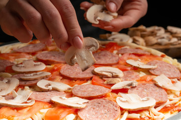 Chef cooks pizza, spreads fresh mushrooms, on the background with ingredients. Recipe book, menu, home cooking. Close up macro