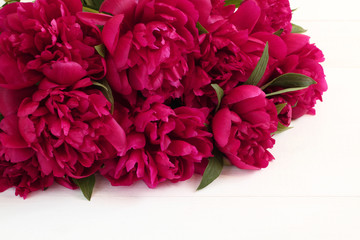 Bouquet of magenta peonies lying on white wooden table. Closeup