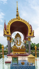 Ko Samui Island, Thailand - March 18, 2019: Wat Laem Suwannaram Chinese Buddhist Temple. Closeup of Lord Ganesha sitting under golden baldachin with green foliage and blue sky in back. © Klodien