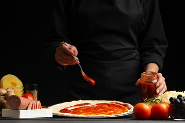 Chef smears Italian pizza sauce, on black background