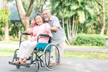 Happy senior woman in a wheelchair walking with her husband
