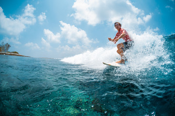 Young caucasian man surfs the ocean wave and makes a lot of splashes into the camera. Chickens surf spot in Maldives - obrazy, fototapety, plakaty