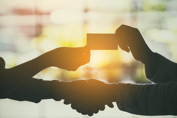 Silhouette image of two people shaking hands and exchanging empty business card