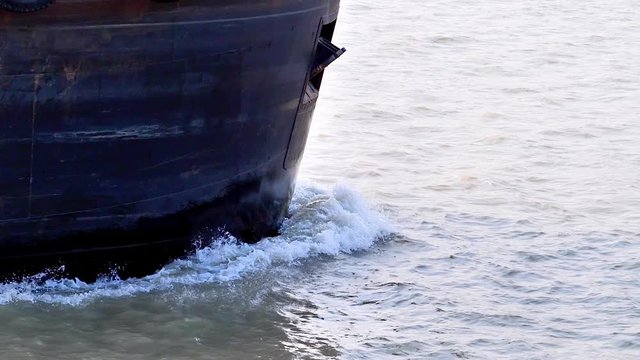 Close up of the ship's prow sailing in river.  The nose of the cargo ship cuts the water creating small waves on the water. Super slow motion.