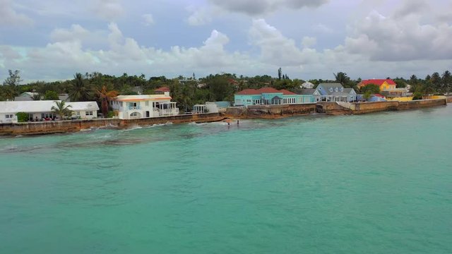 Aerial: Three People Swimming Near Waterfront Homes in Choppy Tropical Water - Nassau, Bahamas