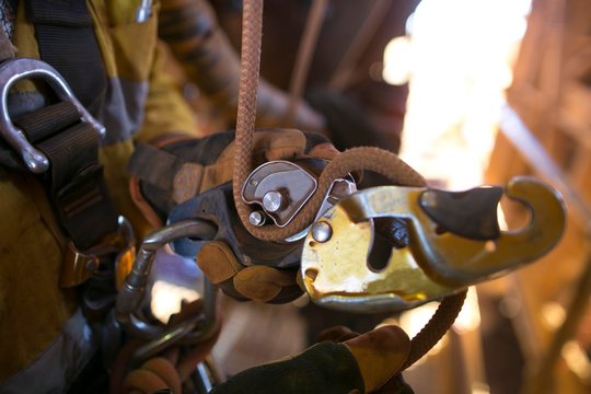 Picture of rope access technician hand opening descender and clipping connecting inserting with 10 MM low stretch Nylon abseiling rope attached into safety harness loop in locking positioning 