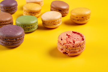 broken pink macaroon on yellow background with  different colors macaroon on back