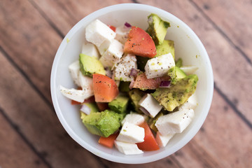healthy salad from fresh vegetables with avocado, tomatoes and fresh mozzarella cheese served in white bowl