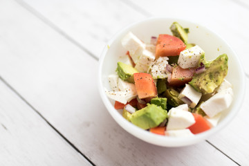 healthy salad from fresh vegetables with avocado, tomatoes and fresh mozzarella cheese served in white bowl