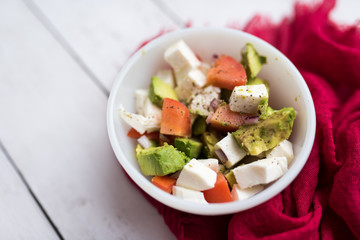 healthy salad from fresh vegetables with avocado, tomatoes and fresh mozzarella cheese served in white bowl