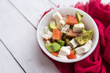 healthy salad from fresh vegetables with avocado, tomatoes and fresh mozzarella cheese served in white bowl