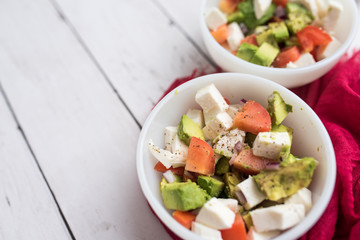 healthy salad from fresh vegetables with avocado, tomatoes and fresh mozzarella cheese served in white bowl