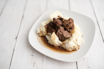 Beef tips with gravy on mashed potatoes served on white plate