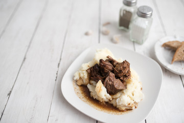 Beef tips with gravy on mashed potatoes served on white plate