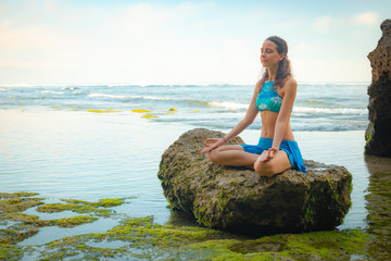 Young woman sitting on the rock, meditating, practicing yoga and pranayama at the beach, Bali. Hands in gyan mudra - Powered by Adobe