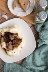 Beef tips with gravy on mashed potatoes served on white plate