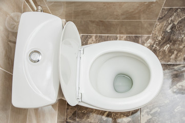 Clean ordinary white toilet in the interior with brown marble tiles.