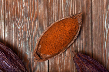 Cacao powder in a natural cocoa pod on a old wooden background. Top view.