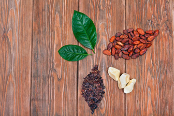 Two green leaves and two leaves made of cocoa beans and nibs and cacao butter on a wooden background. Top view. Text space. 