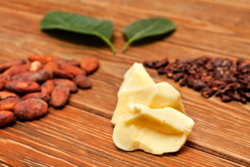 Cacao butter, two leaves made of cocoa beans and cacao nibs and green leaves on wooden background. 