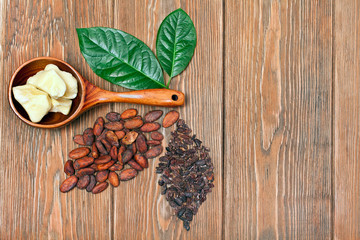 Cocoa butter in wooden spoon with green leaves. And two leaves made of cocoa beans and cacao nibs on wooden background. Top view. Text space.
