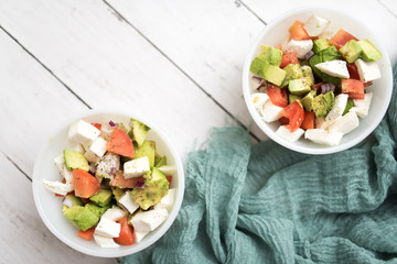 healthy salad from fresh vegetables with avocado, tomatoes and fresh mozzarella cheese served in white bowl