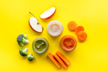 Baby food. Colorful puree in glass jars near vegetables and fruits on yellow background top view