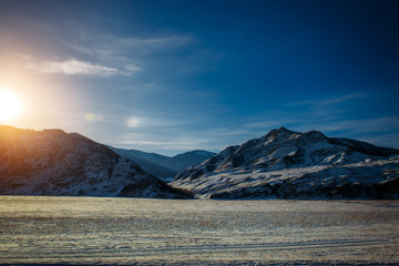 Fototapeta premium Fantastic panorama of snow-covered plains and mountain slopes covered with snow on a frosty sunny winter day. Wild and desert places, road trips, Siberian expanses.