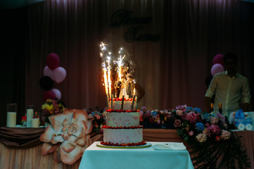 Wedding cake with burning sparklers in a darkened festive hall. Large cake decorated with figures of bride and groom. Culmination of wedding celebration. Pyrotechnics at the wedding.