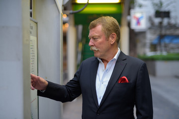 Profile view of handsome senior businessman with mustache checking the map in the city