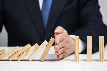 Male hand stopping the domino effect. Risk control concept.