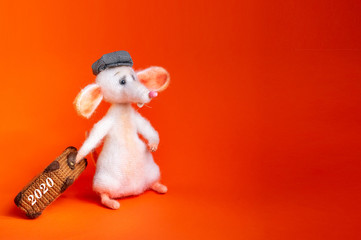 White, knitted mouse with a suitcase in his paw, in a plaid cap. The symbol of the two thousand twentieth year. Isolated bright orange background