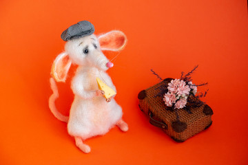 A white knitted mouse in plaid cap, with cheese in its paws. In background, in selected focus, ...