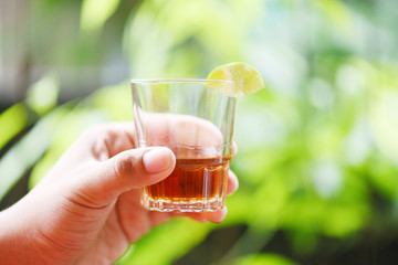 Hand man holding glasses of whiskey or alcohol drink with lemon lime and nature background