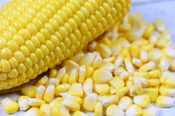 Peeled ear of corn on the cob and corn seeds on white wooden