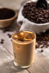 Glass of mocha latte ice coffee espresso with ingredients, whole roasted beans, scoop, grind, bag on wood 