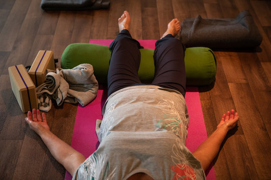 View from above photo of an adult female lying on top of a yoga mat on the floor while having her arms