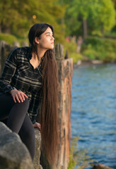 Biracial young woman sitting  looking out over lake at sunset