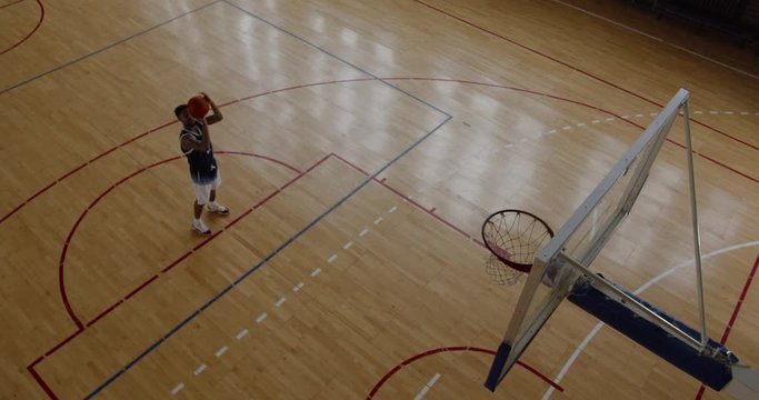 OVERHEAD HIGH ANGLE JIB SHOT African American black college male basketball player practicing shots alone on the indoor court. 4K UHD 50 FPS SLOW MOTION RAW Graded footage