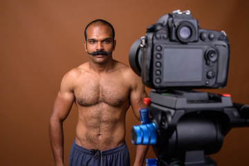 Portrait of muscular Indian man with mustache shirtless vlogging with camera