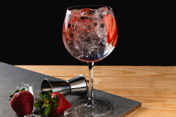 Gin tonic strawberry with juniper stone background in gray color.