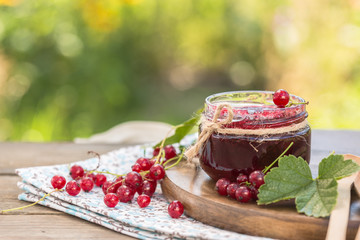 red currant jam and red currant with leaves on a wooden background.