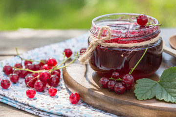 red currant jam and red currant with leaves on a wooden background.