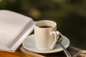 cup of coffee and open book on wooden natural outdoor table