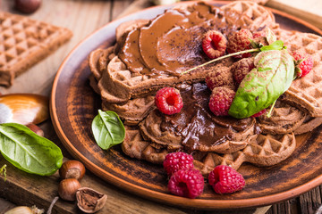 Belgium waffles heart with chocolate sauce raspberries on wood background.