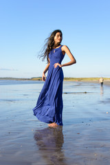 Beautiful model at the beach in Sligo in Ireland. Mixed race Portuguese Indian female model posing. Blue dress, hair flying in the wind. Reflection in the wet sand. Brown hair model. Irish coastline.