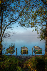 on a lake some rowboats are moored and on the lake there is fog and the lake is quite calm