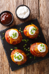 Grilled volcano potatoes wrapped in bacon topped with cheese and sour cream close-up. Vertical top view